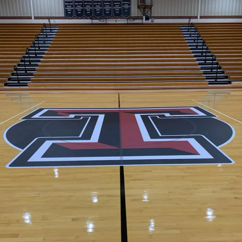 Center court floor logo installation featuring a branded ‘T’ design on hardwood basketball flooring