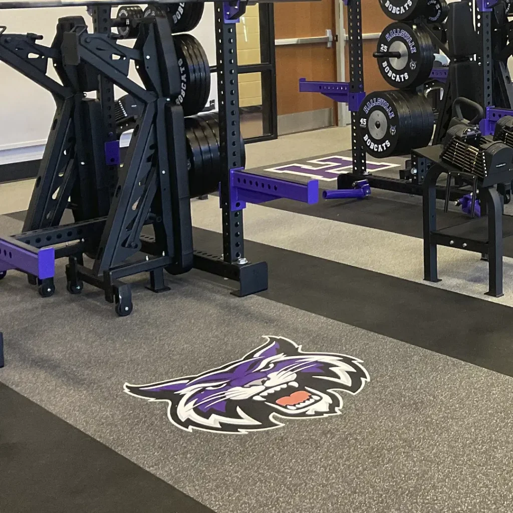 Hallsville High School Bobcats engineered floor logo installed on rubber flooring, with portions of two racks and branded bumper plates also installed by our team.
