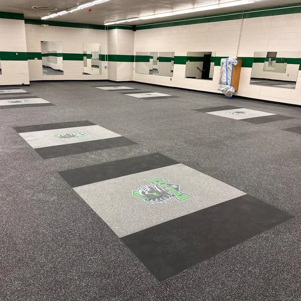 Wide view of a rack-free weightroom featuring multiple East Valley Knights engineered floor logos installed on performance rubber flooring with integrated inlaid platforms, all completed by our team.