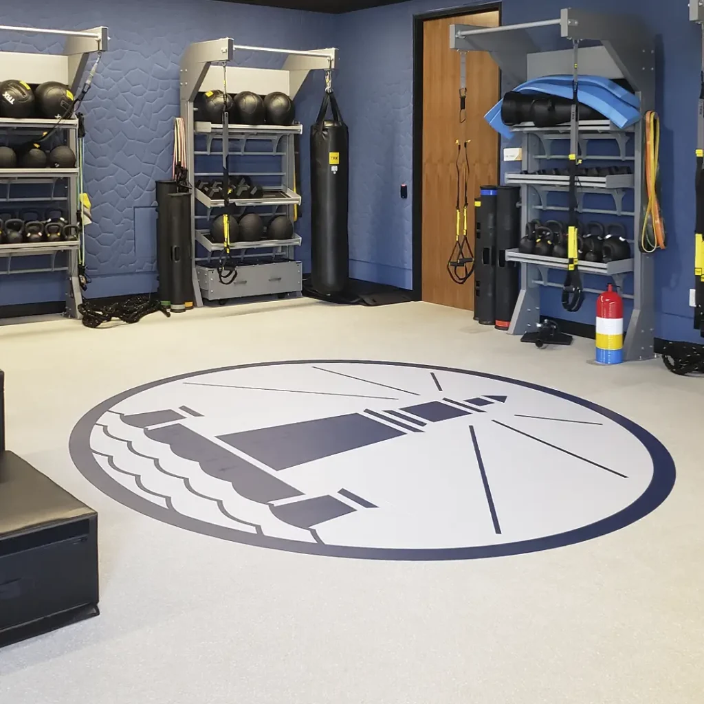 Large engineered floor logo of a lighthouse installed at the center of a room equipped with three TRX storage racks.