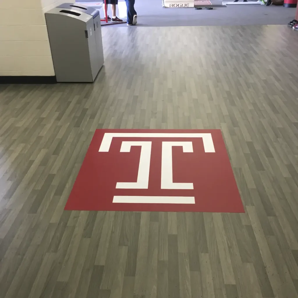 White “T” engineered floor logo inside a red square installed on LVT vinyl flooring.