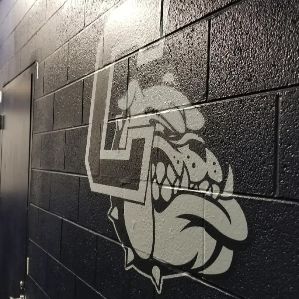 Close-up engineered wall graphic featuring a bold “C” and bulldog logo installed on a dark navy painted block wall.