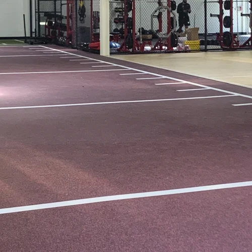 Performance rubber flooring in Rally Maroon with white hash marks installed next to an LVT vinyl flooring section, installed by our American Platforms team.